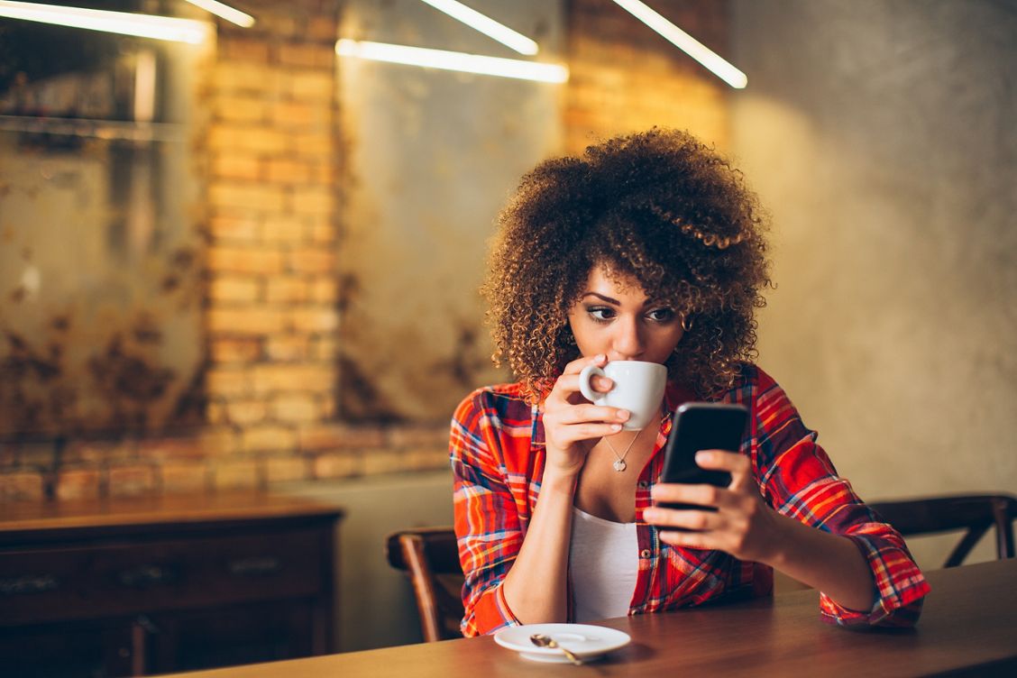 Vrouw drinkt koffie en kijkt op haar zakelijke iPhone.